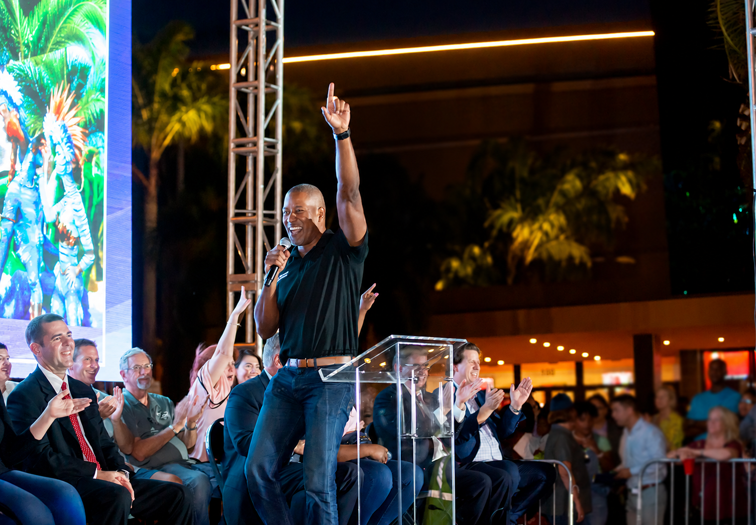 Julio Guzman addressing a community gathering with his hand raised